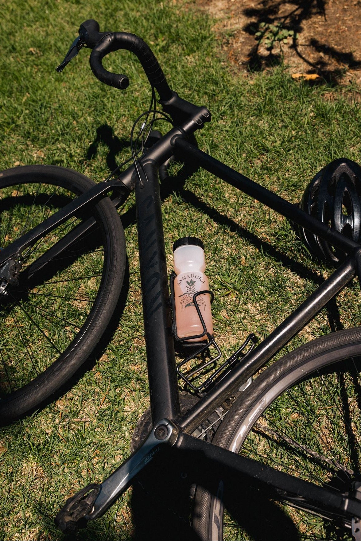 Black bicycle with Sanadora water bottle leaning on grass