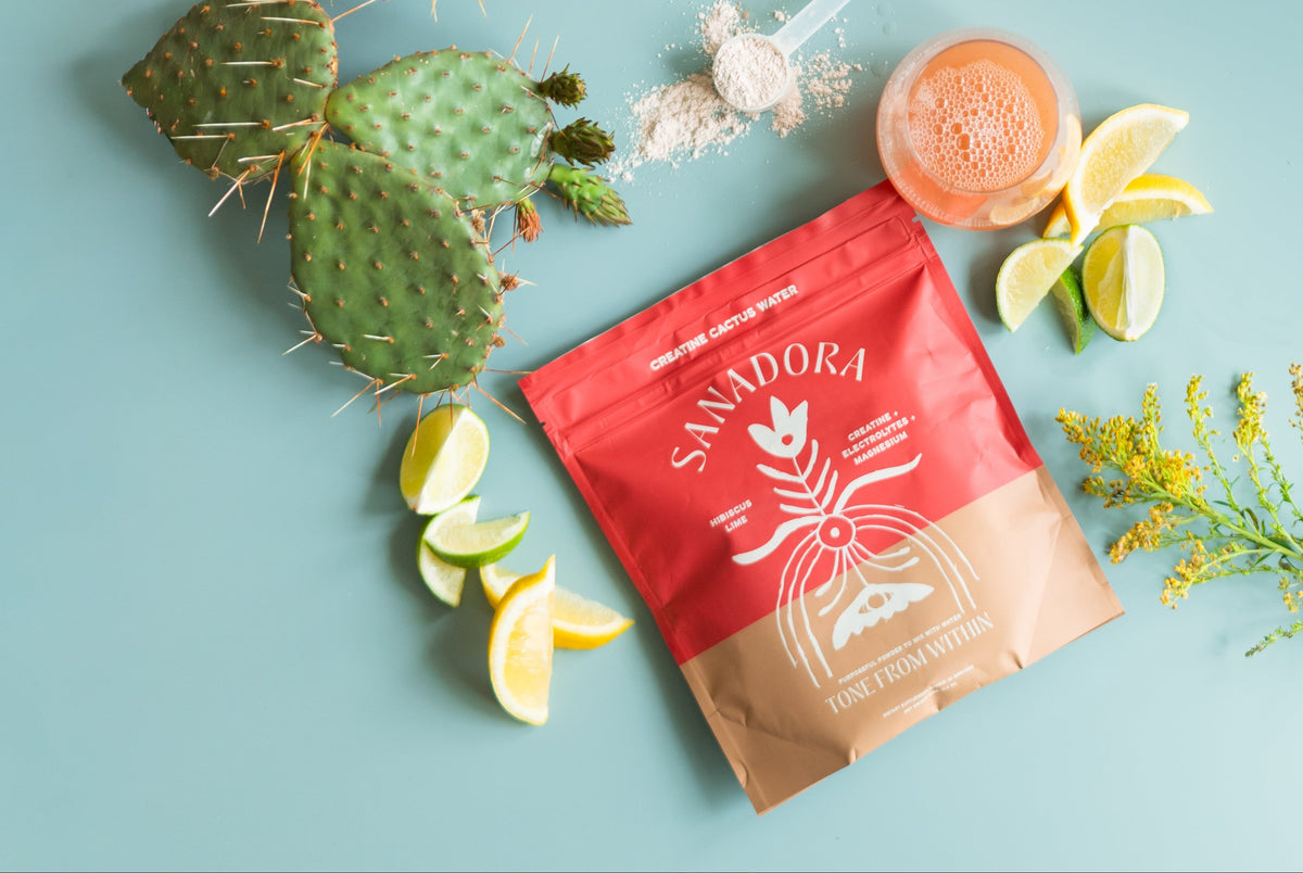 Sanadora Creatine Cactus Water with cactus, lemon, and flowers on a light blue background